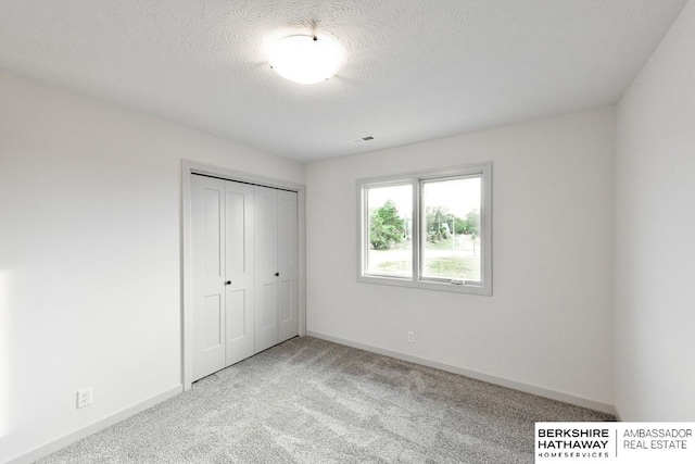 unfurnished bedroom featuring light carpet, a textured ceiling, and a closet