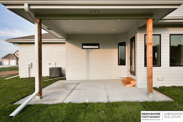 view of exterior entry featuring a lawn, central AC, and a patio