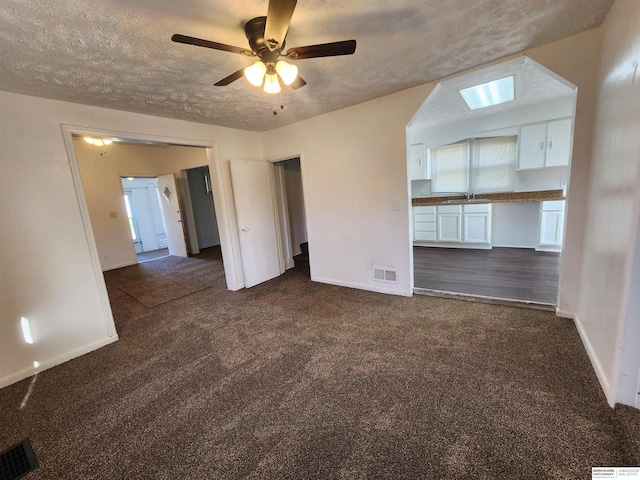 empty room with a skylight, a textured ceiling, sink, ceiling fan, and dark colored carpet