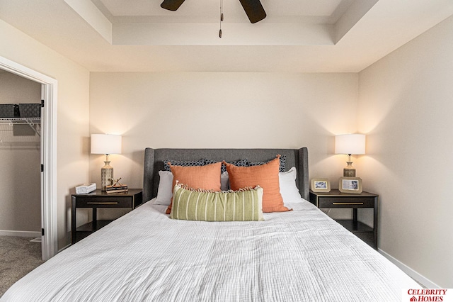 carpeted bedroom with a tray ceiling, a spacious closet, ceiling fan, and a closet