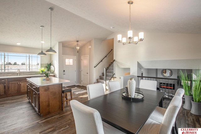 dining area with a fireplace, an inviting chandelier, vaulted ceiling, sink, and dark hardwood / wood-style floors