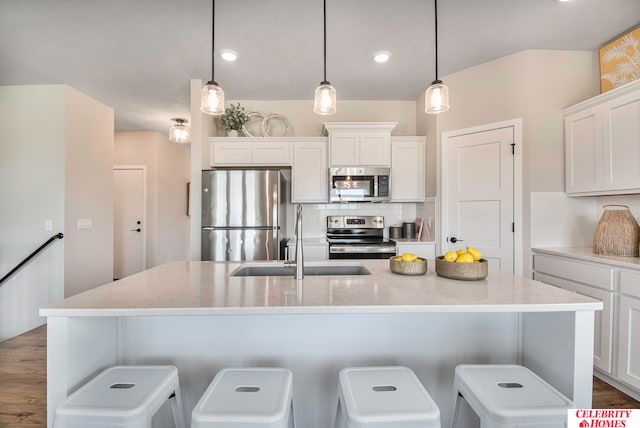 kitchen featuring appliances with stainless steel finishes, a center island with sink, white cabinets, and pendant lighting