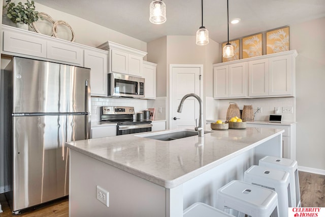 kitchen with pendant lighting, an island with sink, stainless steel appliances, sink, and white cabinets