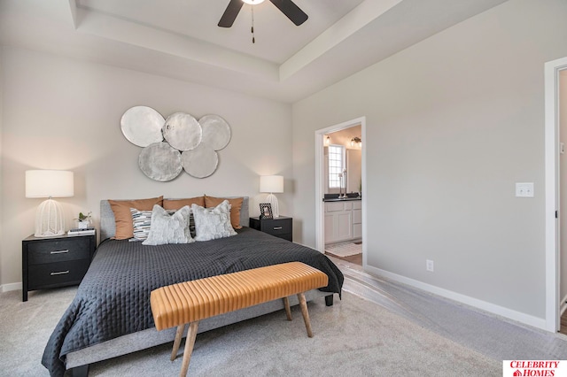 carpeted bedroom featuring a tray ceiling, ceiling fan, and ensuite bath