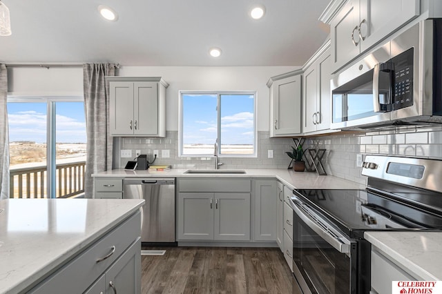 kitchen featuring stainless steel appliances, sink, light stone countertops, dark wood-type flooring, and gray cabinetry