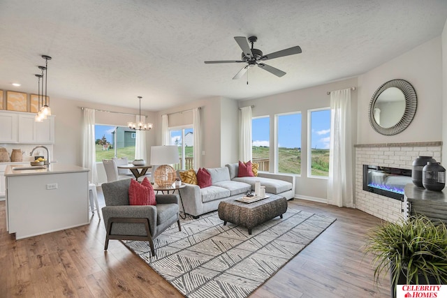 living room featuring light wood-type flooring, ceiling fan with notable chandelier, a fireplace, and a textured ceiling