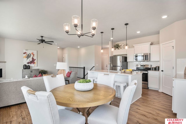 dining area featuring sink, ceiling fan with notable chandelier, light hardwood / wood-style floors, and a brick fireplace