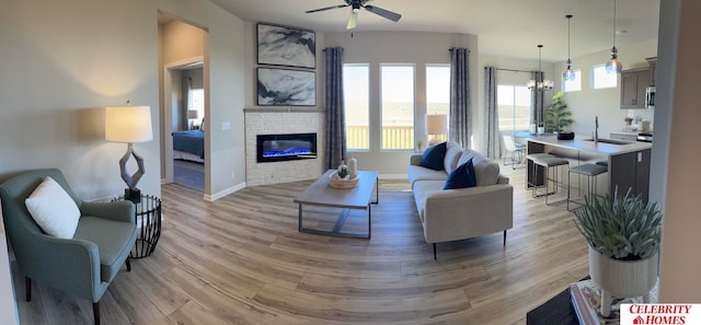 living room featuring ceiling fan with notable chandelier, a fireplace, light hardwood / wood-style flooring, and sink