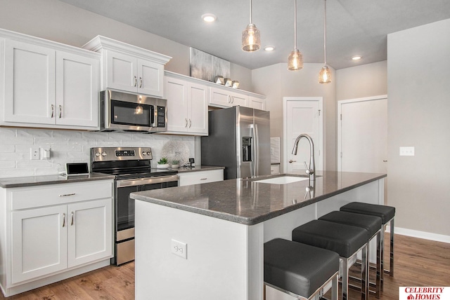 kitchen with white cabinets, stainless steel appliances, light hardwood / wood-style floors, and a kitchen island with sink