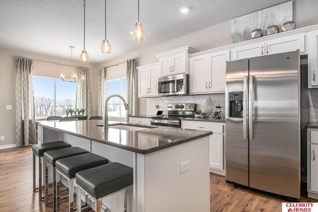 kitchen with a kitchen island with sink, light wood-type flooring, stainless steel appliances, sink, and white cabinets