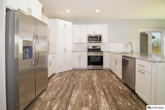 kitchen featuring light stone counters, sink, kitchen peninsula, white cabinetry, and appliances with stainless steel finishes