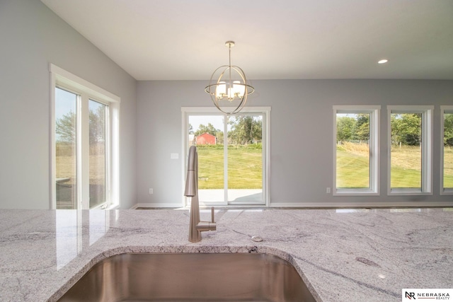 kitchen with pendant lighting, light stone counters, a chandelier, and sink