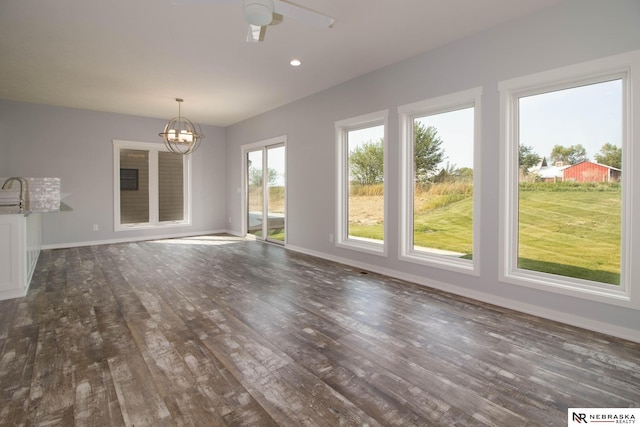 unfurnished living room with ceiling fan with notable chandelier and dark hardwood / wood-style flooring