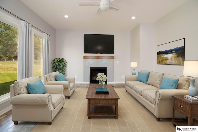 living room with light wood-type flooring, a tiled fireplace, and ceiling fan