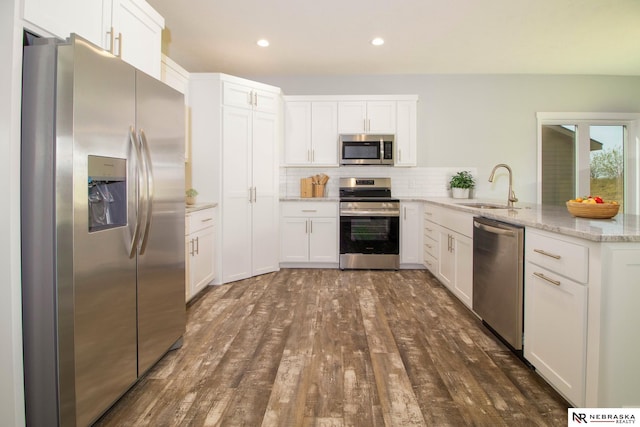 kitchen with sink, white cabinetry, appliances with stainless steel finishes, dark hardwood / wood-style flooring, and light stone countertops