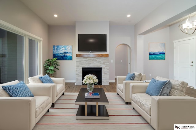 living room featuring light wood-type flooring, a stone fireplace, and an inviting chandelier