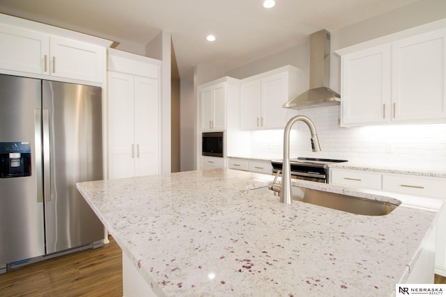 kitchen featuring white cabinetry, light stone counters, wall chimney exhaust hood, hardwood / wood-style flooring, and stainless steel refrigerator with ice dispenser