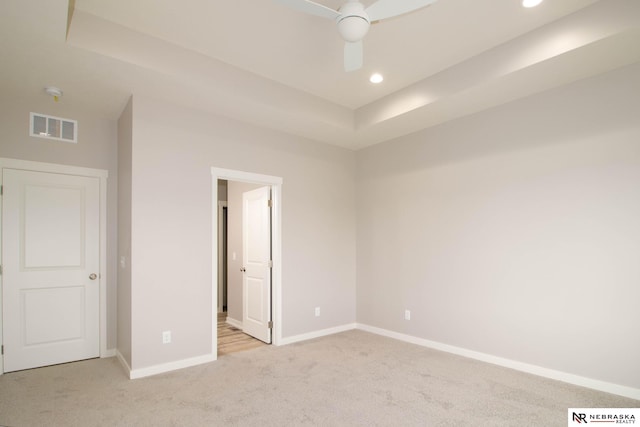 unfurnished bedroom featuring light carpet, a tray ceiling, and ceiling fan