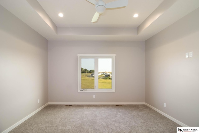 carpeted spare room featuring a raised ceiling and ceiling fan