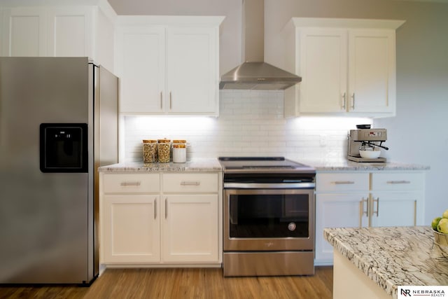 kitchen with appliances with stainless steel finishes, light wood-type flooring, wall chimney range hood, and white cabinetry