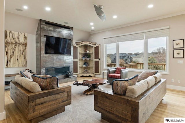 living room with a tiled fireplace, crown molding, and light hardwood / wood-style flooring