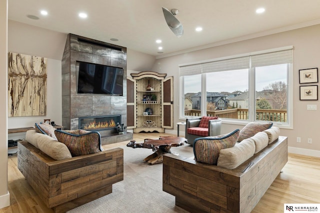 living room with a tiled fireplace, ornamental molding, and light hardwood / wood-style flooring