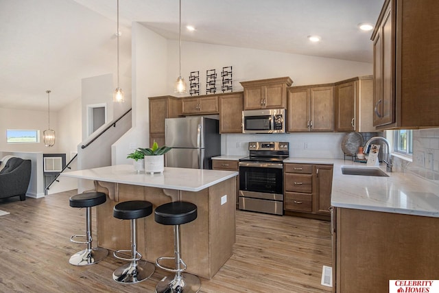 kitchen with light wood-type flooring, backsplash, a kitchen island, sink, and appliances with stainless steel finishes