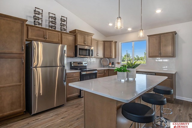 kitchen featuring vaulted ceiling, decorative light fixtures, dark hardwood / wood-style flooring, a center island, and stainless steel appliances