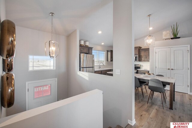 hall with lofted ceiling, light hardwood / wood-style flooring, sink, and a notable chandelier