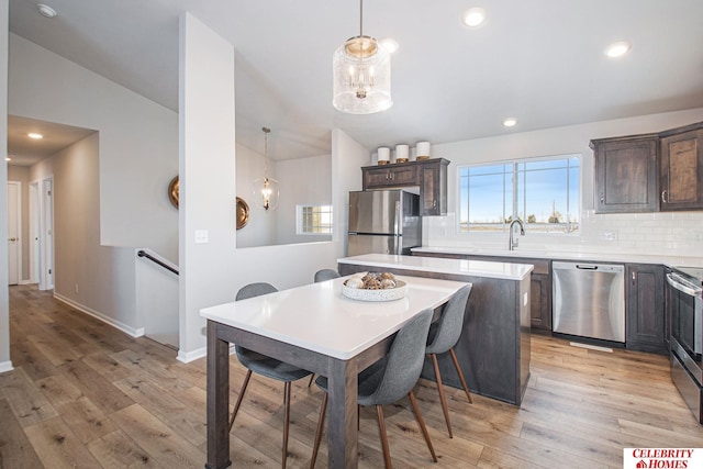 kitchen with appliances with stainless steel finishes, plenty of natural light, decorative light fixtures, and light hardwood / wood-style floors