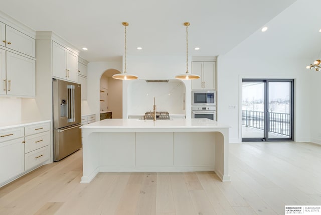 kitchen featuring light wood-type flooring, an island with sink, stainless steel appliances, and light countertops