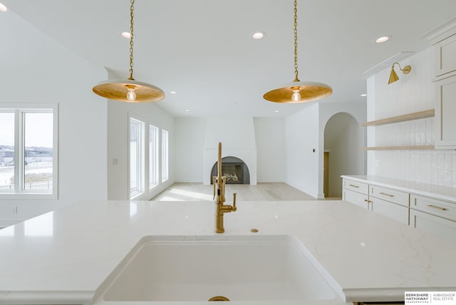 kitchen featuring recessed lighting, hanging light fixtures, light stone counters, a sink, and open floor plan