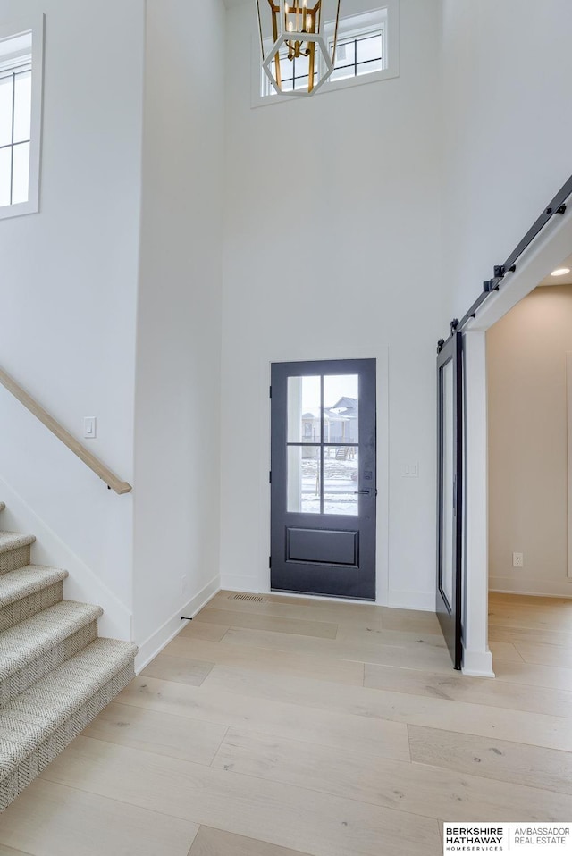 foyer featuring an inviting chandelier, a towering ceiling, a barn door, and light wood-style flooring