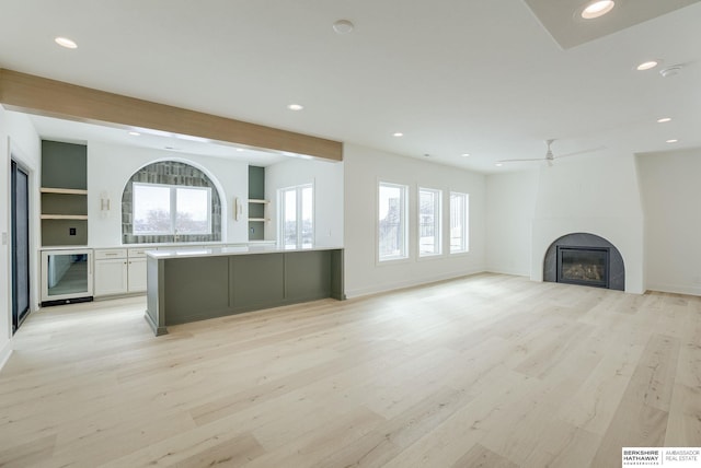 unfurnished living room with a fireplace, light wood finished floors, a wealth of natural light, and beverage cooler