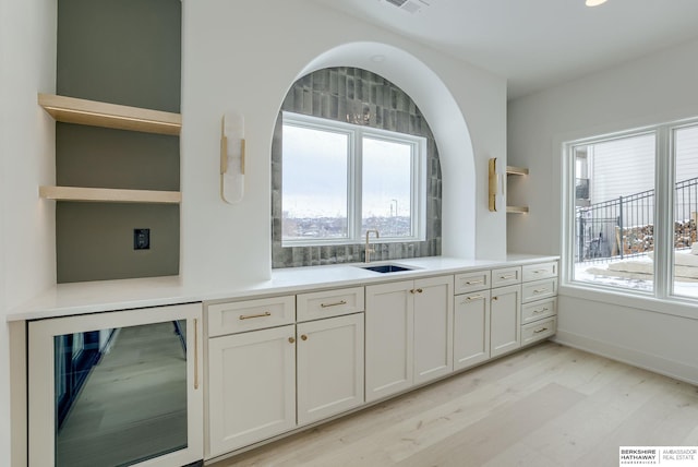 kitchen featuring open shelves, light wood-style floors, a sink, white cabinetry, and wine cooler