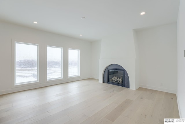 unfurnished living room featuring recessed lighting, light wood-style flooring, and a glass covered fireplace