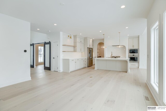 kitchen with white cabinetry, visible vents, stainless steel appliances, light wood-style floors, and arched walkways