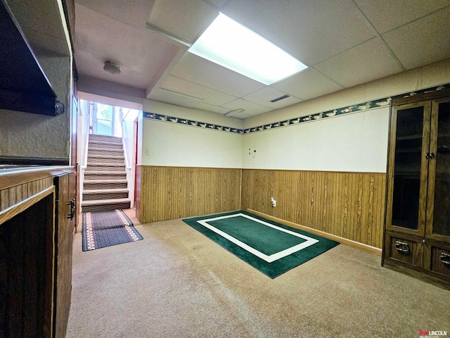 interior space with a drop ceiling, wood walls, and carpet floors