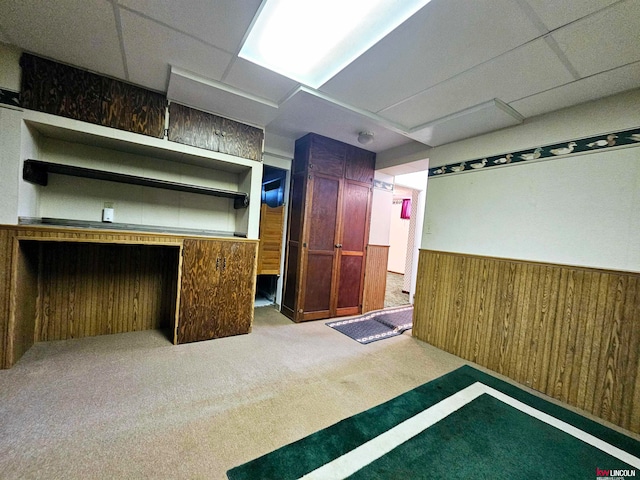 basement with a paneled ceiling, light colored carpet, and wooden walls