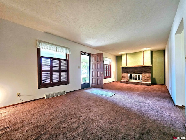 unfurnished living room featuring a textured ceiling, a brick fireplace, and dark colored carpet