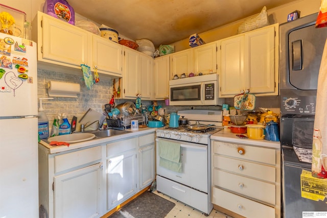 kitchen with white appliances, sink, decorative backsplash, stacked washing maching and dryer, and white cabinets