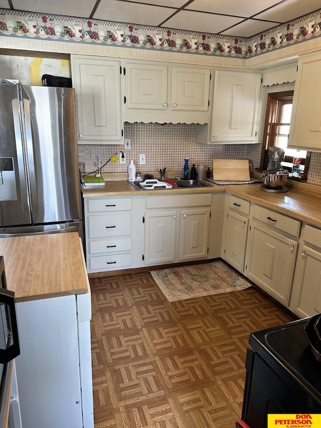 kitchen with sink, a paneled ceiling, stainless steel refrigerator with ice dispenser, black electric range, and decorative backsplash