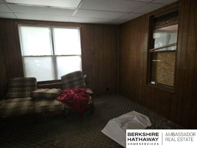 sitting room featuring wooden walls, a paneled ceiling, and carpet flooring