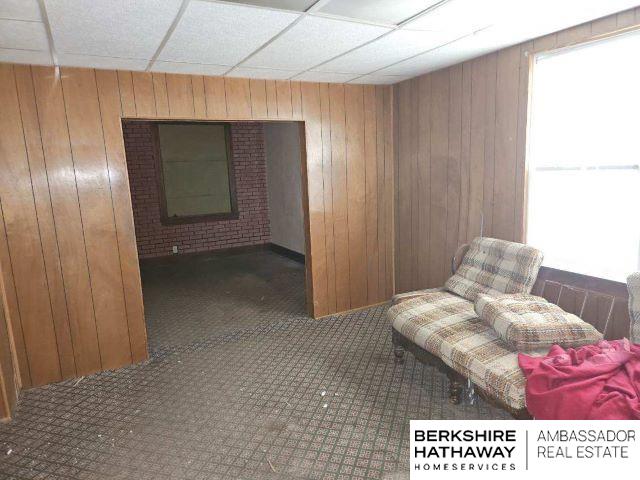 sitting room with dark carpet, wood walls, and a paneled ceiling