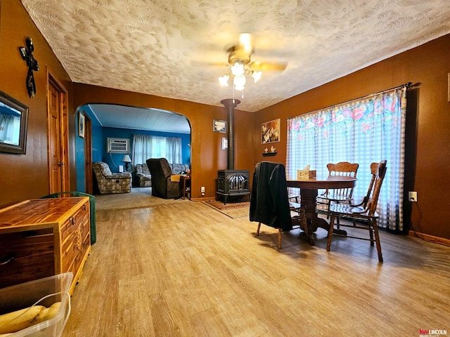 dining space featuring a wood stove, a textured ceiling, ceiling fan, a wall unit AC, and light hardwood / wood-style flooring