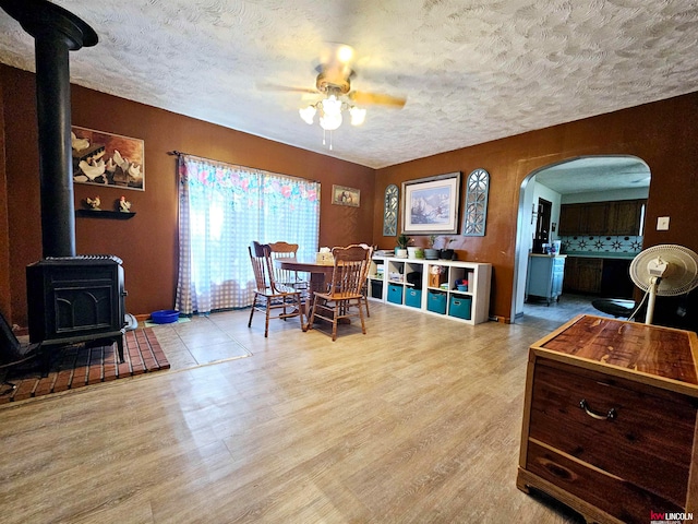 dining area featuring a textured ceiling, light hardwood / wood-style floors, ceiling fan, and a wood stove