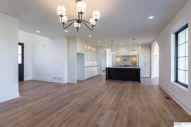 kitchen featuring decorative light fixtures, a center island with sink, white cabinetry, hardwood / wood-style floors, and decorative backsplash