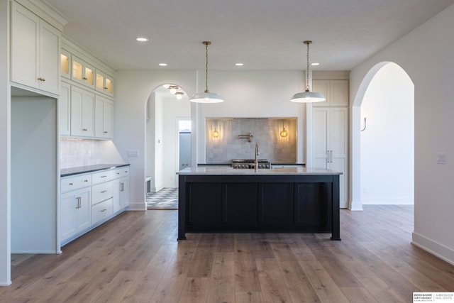 kitchen featuring pendant lighting, light wood-type flooring, a center island with sink, and tasteful backsplash