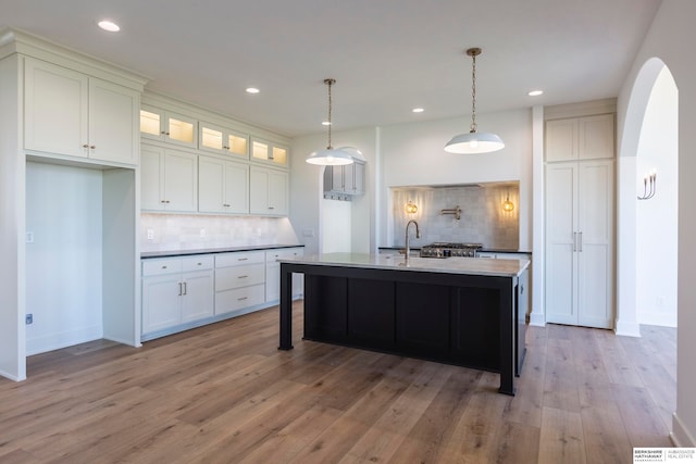 kitchen featuring light wood-type flooring, white cabinetry, a kitchen island with sink, and tasteful backsplash