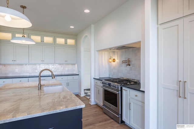 kitchen with decorative backsplash, white cabinets, stainless steel range, and hanging light fixtures